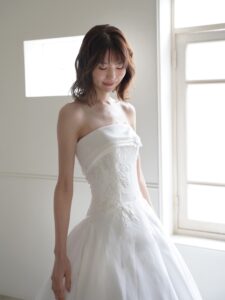 MK-012（オフホワイト）| 独特のとろみがあるトリアセテートミカドをふんだんに使ったAラインのシンプルドレス。スカートの接ぎ線を少なくし、生地の落ち感がスカートのシルエットに表現されるようなカッティングにしました。前中心から後ろにかけて切り替え位置を低くした変形ドロップウエストで、前中心は下にすっきり落ちるデザインでお腹のふくらみをカバーし、脇からボリュームを出すことで華奢なウエストを強調するパターンにこだわった１着です