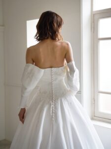 MK-012（オフホワイト）| 独特のとろみがあるトリアセテートミカドをふんだんに使ったAラインのシンプルドレス。スカートの接ぎ線を少なくし、生地の落ち感がスカートのシルエットに表現されるようなカッティングにしました。前中心から後ろにかけて切り替え位置を低くした変形ドロップウエストで、前中心は下にすっきり落ちるデザインでお腹のふくらみをカバーし、脇からボリュームを出すことで華奢なウエストを強調するパターンにこだわった１着です