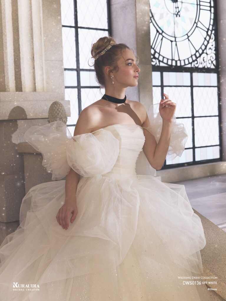 DWS0136 Blue / Off White 「Cinderella」| 「シンデレラ」の魔法にかけられる煌めきを、2種類のグリッターチュールを贅沢に重ね合わせて表現した、ロマンティックな一着 です。「シンデレラ」の衣装からインスパイアされたボリュームのあるタッキングスカートでモードな一面もあります。リボン風の ボリュームショルダーが愛らしさもプラスするプリンセスドレスです。※袖は取り外し可能です。