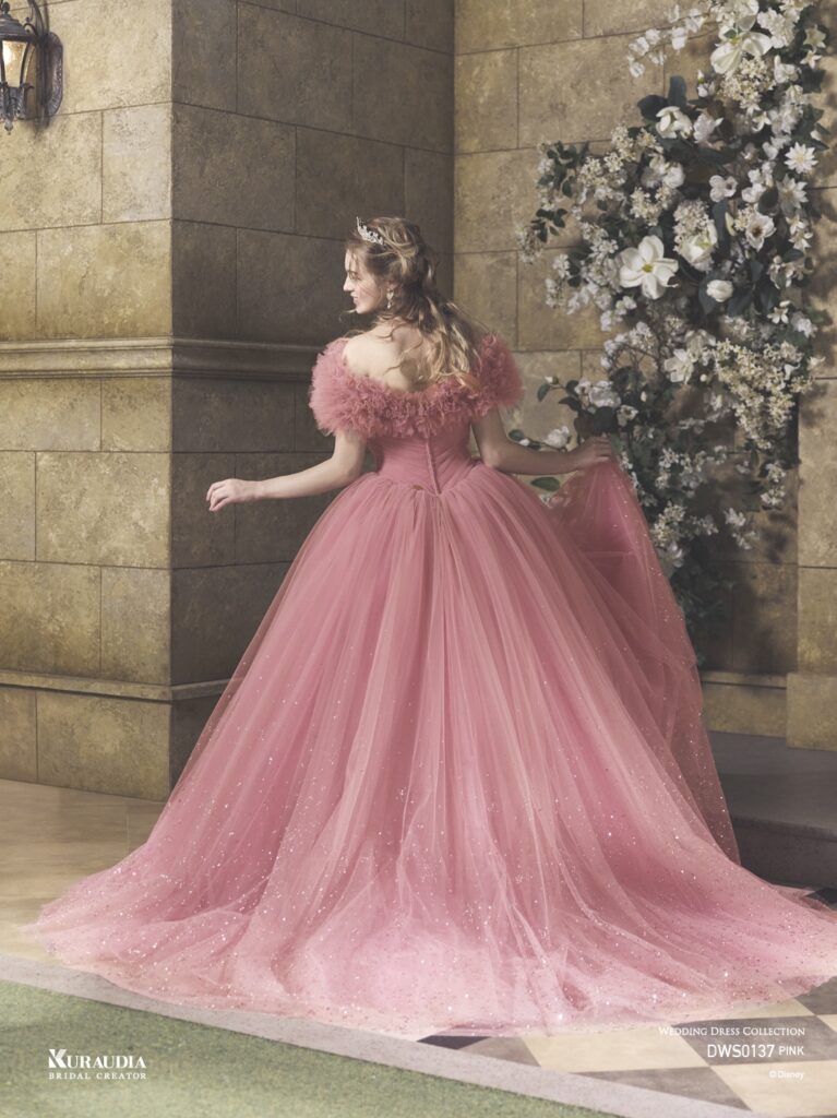 DWS0137 Pink 「Princess Aurora」| 「オーロラ姫」からインスパイアされたエレガントで女性らしいローズピンクのチュールドレスです。肩にのるフリルケープや、 ローズをイメージしたスパンコールのモチーフがポイントです。ローウエストのV字切り替えでシルエットをより美しく演出し、 スカートには魔法がかかったようなグリッターが煌めき、上品な印象に。※ケープは取り外し可能です。