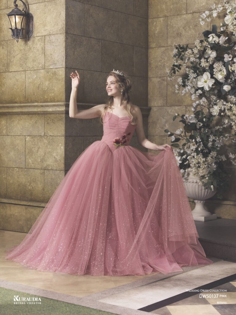 DWS0137 Pink 「Princess Aurora」| 「オーロラ姫」からインスパイアされたエレガントで女性らしいローズピンクのチュールドレスです。肩にのるフリルケープや、 ローズをイメージしたスパンコールのモチーフがポイントです。ローウエストのV字切り替えでシルエットをより美しく演出し、スカートには魔法がかかったようなグリッターが煌めき、上品な印象に。※ケープは取り外し可能です。