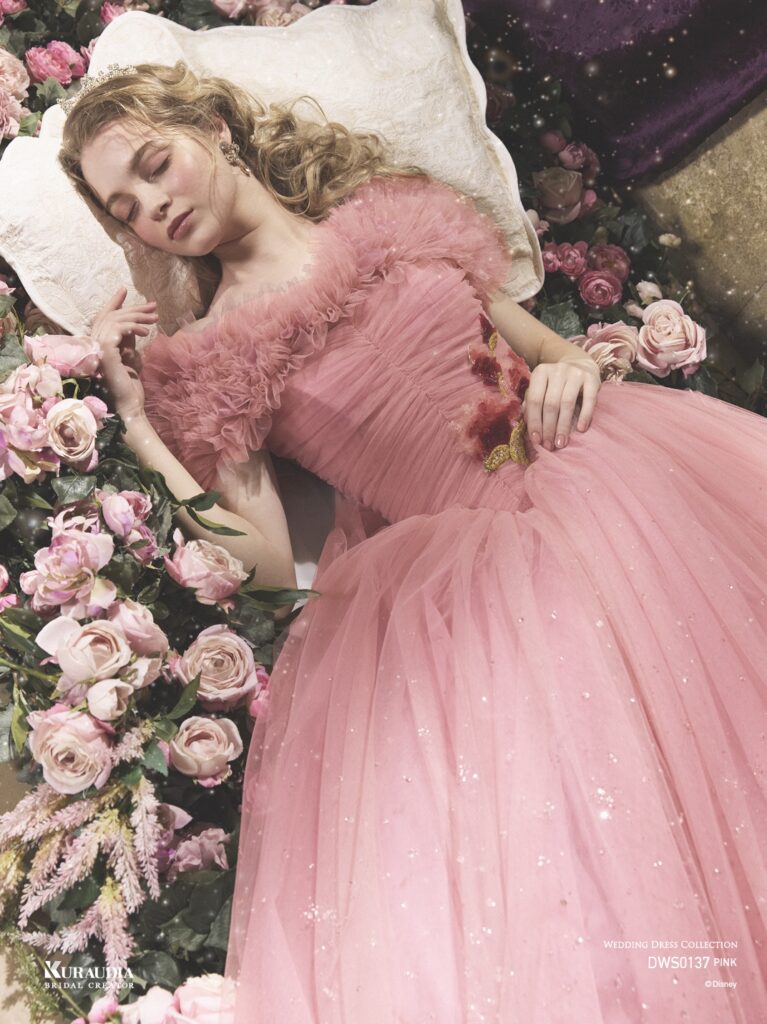 DWS0137 Pink 「Princess Aurora」| 「オーロラ姫」からインスパイアされたエレガントで女性らしいローズピンクのチュールドレスです。肩にのるフリルケープや、 ローズをイメージしたスパンコールのモチーフがポイントです。ローウエストのV字切り替えでシルエットをより美しく演出し、スカートには魔法がかかったようなグリッターが煌めき、上品な印象に。※ケープは取り外し可能です。