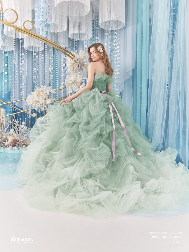 DWS0138 Blue Green 「Ariel」| 波のゆらめきを表現したタッキングのスカートがポイントの、「アリエル」からインスパイアされたボリュームドレスです。 ブルーグリーンの美しいグラデーションと、パープルのウエストリボンが「アリエル」らしいカラーリングです。バルーンデザインの裾やタッキングのスカートの内側からは海の中の光をイメージしたグリッターが光輝きます。動きのある立ち上がったドレープ身頃には海の泡を表現したパールやビーズがあしらわれています。