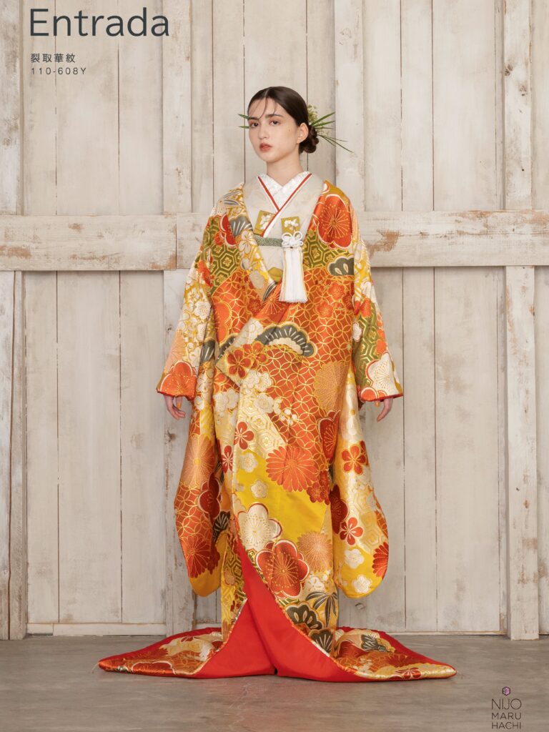 色打掛 110-608Y | 裂取という直線的な形で地を様々な文様、色に分け、その上に意匠化した梅や菊をあしらいました。梅は新春に寒さに先駆けて咲くことから春を告げる花とされており、菊は長寿の意味をもち、古くより愛されています。地には和が重なり、広がる様から別名「和繋ぎ文」と言われ永遠をあらわす七宝、亀の甲羅をデザインした亀甲といった吉祥文様をあしらい、織物にはめずらしくも染分けのように様々な色をあしらい晴れの日を彩るにぴったりの一枚が完成しました。