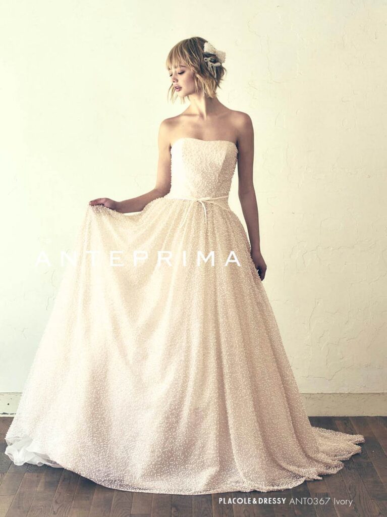 ANT0367（アイボリー/オレンジ） | ジュエルパールグリッターの輝きを全身にまとい、上品さと可憐さをあわせ持つ“現代のプリンセス”を表現。新素材“エアーファブリックオーガン”が、ふんわりと空気を含んだような軽やかなドレープを描きます。ピーチオレンジのやさしい色合いが肌にやわらかく映え、見る人にぬくもりと幸せを届けるような一着です。