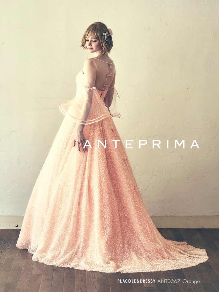 ANT0367（アイボリー/オレンジ） | ジュエルパールグリッターの輝きを全身にまとい、上品さと可憐さをあわせ持つ“現代のプリンセス”を表現。新素材“エアーファブリックオーガン”が、ふんわりと空気を含んだような軽やかなドレープを描きます。ピーチオレンジのやさしい色合いが肌にやわらかく映え、見る人にぬくもりと幸せを届けるような一着です。