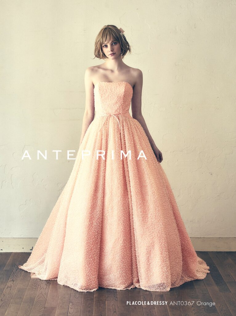 ANT0367（アイボリー/オレンジ） | ジュエルパールグリッターの輝きを全身にまとい、上品さと可憐さをあわせ持つ“現代のプリンセス”を表現。新素材“エアーファブリックオーガン”が、ふんわりと空気を含んだような軽やかなドレープを描きます。ピーチオレンジのやさしい色合いが肌にやわらかく映え、見る人にぬくもりと幸せを届けるような一着です。