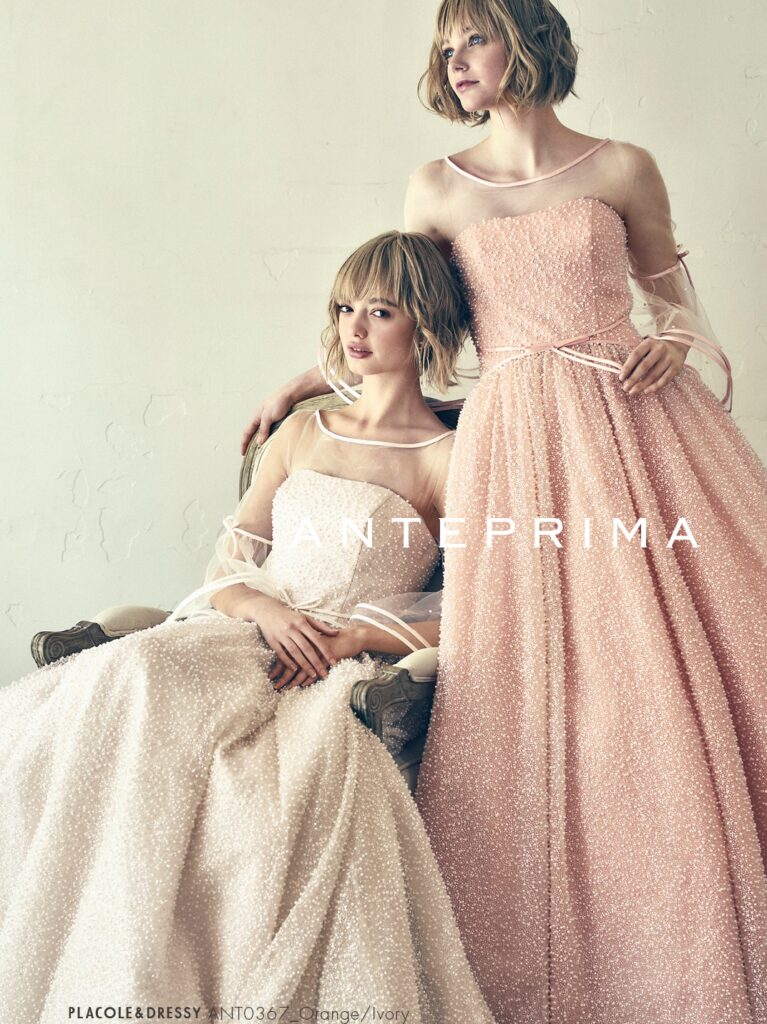 ANT0367（アイボリー/オレンジ） | ジュエルパールグリッターの輝きを全身にまとい、上品さと可憐さをあわせ持つ“現代のプリンセス”を表現。新素材“エアーファブリックオーガン”が、ふんわりと空気を含んだような軽やかなドレープを描きます。ピーチオレンジのやさしい色合いが肌にやわらかく映え、見る人にぬくもりと幸せを届けるような一着です。