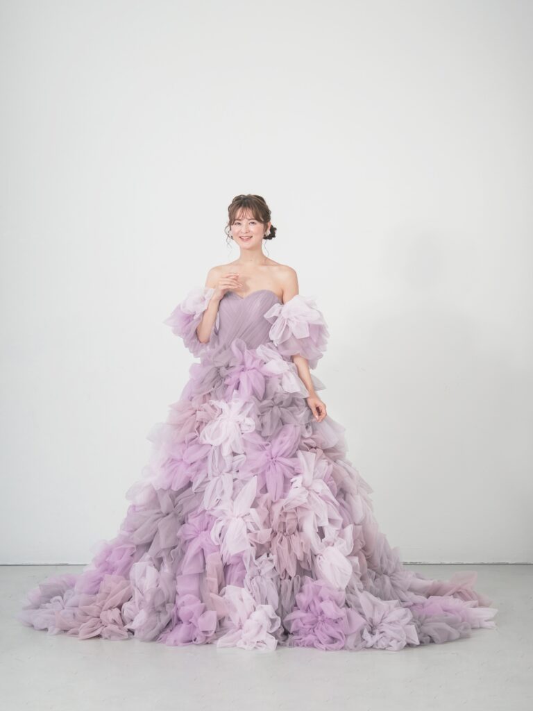 LQ-027（ラベンダー） | 柔らかいピンク・ラベンダーの色を複数混ぜ合わせてひとつずつふんわりと、立体的に形成したハンドメイドフラワーをそのまま身に纏うようなフォトジェニックなドレス。花びらを一枚一枚つまんでふんわり見せる工程や、お花中心のクリスタルをチュールでくるむ技法などよく見るととっても繊細な手仕事でできているのがわかります。