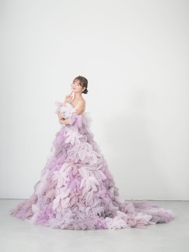 LQ-027（ラベンダー） | 柔らかいピンク・ラベンダーの色を複数混ぜ合わせてひとつずつふんわりと、立体的に形成したハンドメイドフラワーをそのまま身に纏うようなフォトジェニックなドレス。花びらを一枚一枚つまんでふんわり見せる工程や、お花中心のクリスタルをチュールでくるむ技法などよく見るととっても繊細な手仕事でできているのがわかります。