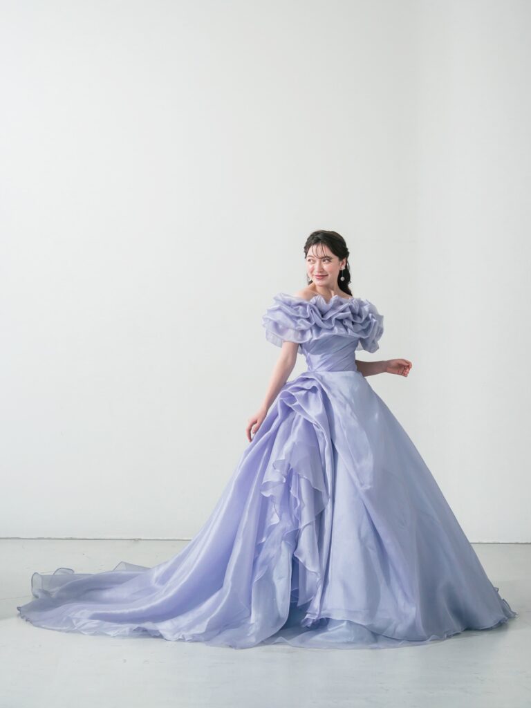 ST-111 | やわらかなウィスティリアカラーが空気まで優しく染める一着。透明感のあるオーガンジーの重なりと、流れるようなボリュームシルエットが、動くたびに表情を変えてくれます。 甘すぎず、上品で、記憶に残るカラードレス。静かな華やかさをまといたい花嫁さまへ。