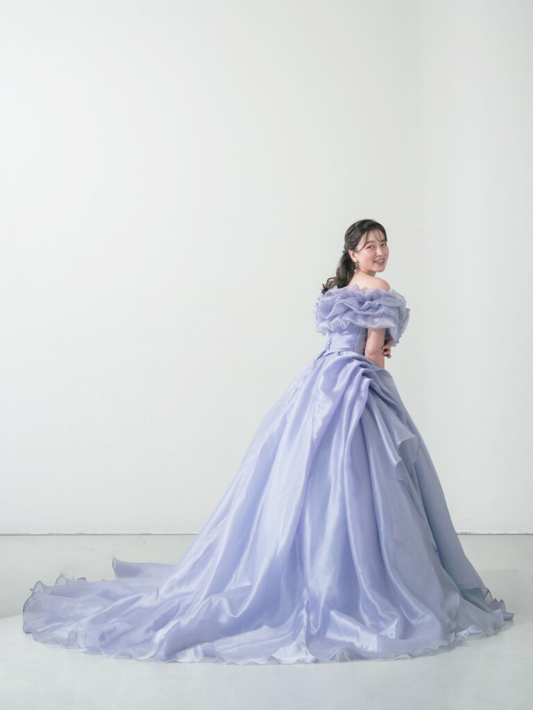 ST-111 | やわらかなウィスティリアカラーが空気まで優しく染める一着。透明感のあるオーガンジーの重なりと、流れるようなボリュームシルエットが、動くたびに表情を変えてくれます。 甘すぎず、上品で、記憶に残るカラードレス。静かな華やかさをまといたい花嫁さまへ。